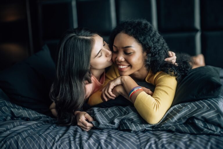 Lesbian partners share joy play on bed embrace exchange tender kiss radiating genuine happiness